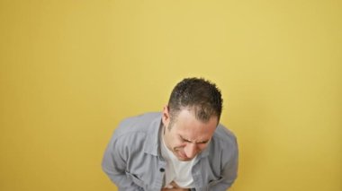 Gömlek giyen İspanyol genç adam mide ağrısı ve mide hastalığıyla boğuşuyor. Karın bölgesindeki ağrıyı gösteren sarı arkaplanda izole halde duruyor.