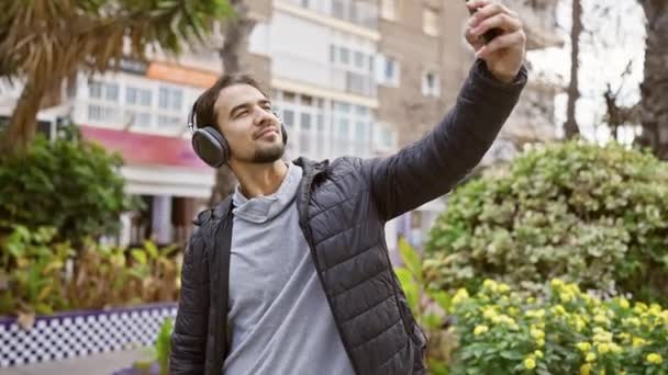 Ein Junger Hispanischer Mann Mit Kopfhörern Macht Ein Selfie Einem — Stockvideo