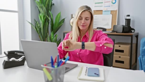 一位穿着粉色衬衫的年轻女性带着笔记本电脑和智能手机在办公室的办公桌前工作 她表达着各种各样的情感 — 图库视频影像