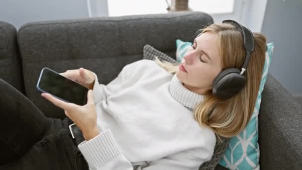 Eine Junge Frau Mit Kopfhörern Entspannt Sich Auf Einer Couch — Stockvideo