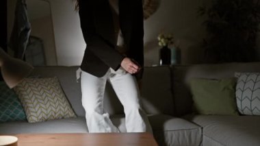 Sıcak bir oturma odasında kırmızı topukluları çıkaran yorgun genç bir kadın.