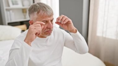 Uykulu orta yaşlı, gri saçlı, pijamalı bir adam, yorgun gözlerini parmaklarıyla açmaya çalışıyor.