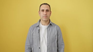 İspanyol gömlekli genç adam şokta, yüzünü ve gözlerini kapayarak utanmış bir ifadeyle parmaklarının arasından bakıyor. izole edilmiş sarı arkaplan
