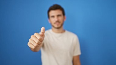 Sakallı genç adam mavi bir duvarın önünde olumlu ve onaylı bir şekilde başparmak kaldırıyor..