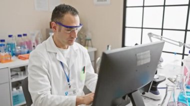 Laboratuvar önlüklü profesyonel bir İspanyol parlak bir laboratuvar ortamında bilgisayar başında çalışıyor..