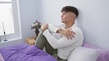 Neşeli, genç, İspanyol bir adam pijamalarıyla uzanmış, rahat yatağından dişlek bir gülümseme sergiliyor.