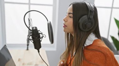 Kulaklık takan genç bir İspanyol kadın kapalı bir stüdyoda mikrofona konuşuyor..