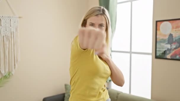 身穿T恤衫的愤怒而咄咄逼人的金发女青年握紧拳头在屋里打拳时表现出敌意 象征着家庭内部的冲突和暴力 — 图库视频影像