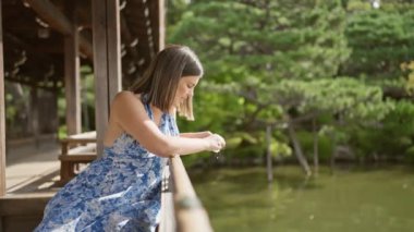 Güzel bir İspanyol kadının büyüleyici portresi doğanın cömertliğinden zevk alıyor, Kyoto 'nun geleneksel türbe parkında sakin bir jingu havuzunda balık besliyor.