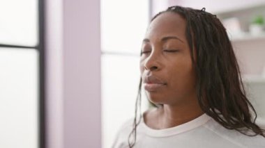 Kıvırcık saçlı, sakin, Afro-Amerikalı bir kadın. Oturma odasında meditasyon yapıyor..