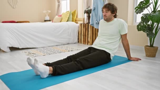 一个悠闲的年轻人坐在明亮的卧室里的瑜伽垫上 四周都是舒适的装饰 — 图库视频影像