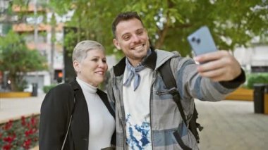 Bir kadın ve bir erkek şehir parkında mutlu bir şekilde selfie çekiyorlar. Arkadaşça ya da ailevi bir bağ sergiliyorlar..