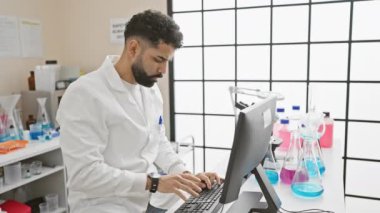 Laboratuvar önlüklü bir adam, parlak bir laboratuvar ortamında bilgisayar üzerinde çalışırken sırt ağrısı yaşar..