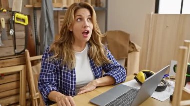 Neşeli genç Latin güzeli, bir numaralı marangozluk kraliçesi, ahşap bir masada otururken parlayan parlak bir gülümseme, başarılı bir Eureka 'yı işaret ediyor, kapalı mekandaki rahat atölyesinde