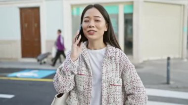 Şehir sokaklarında akıllı telefondan konuşan Çinli bir kadın gülümsüyor..