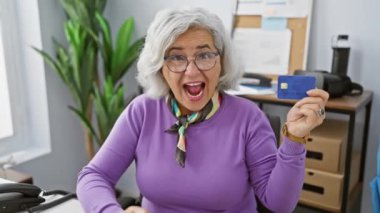 Muzaffer orta yaşlı kadın ofisteki finansal başarısını zaferle kutluyor, sevinçle kredi kartını yükseltiyor.