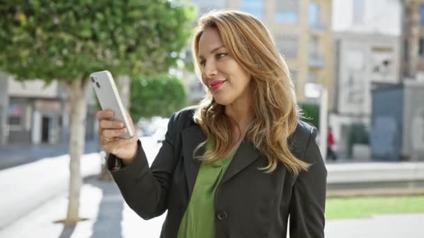 Een Lachende Spaanse Vrouw Een Zakenpak Met Een Smartphone Buiten — Stockvideo