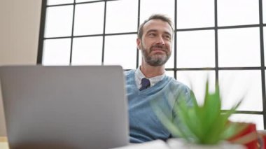 Sakallı, yakışıklı, orta yaşlı bir adam. Ofiste, pencerenin yanında, bilgisayarında ve bitkisinde gülümsüyor..
