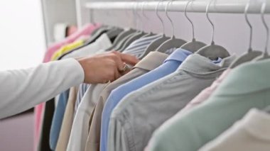 Düzenli, renkli, modern bir gardıropta rafta asılı çeşitli tişörtleri karıştıran bir insan..