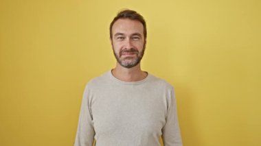 Yakışıklı, orta yaşlı, kendine güvenen, havalı bir tişört giyen, mükemmel, mutlu bir gülümseme sergileyen bir İspanyol. Parlak sarı bir arkaplanda izole edilmiş..