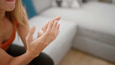 Sarışın bir kadın ellerini kapalı bir yerde muayene ediyor. Kanepenin arkası bulanık. Sakin bir ev ortamını işaret ediyor..