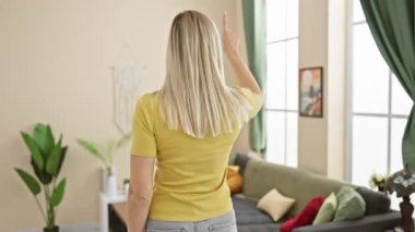 Çekici genç sarışın kadın kendinden emin bir şekilde önünü işaret ediyor, evde tişörtle ters poz veriyor, etkili liderlik portresi çiziyor.