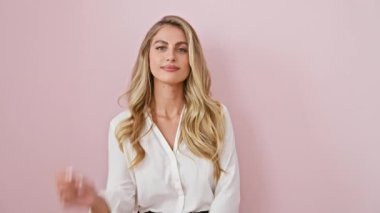 Gururlu ve pozitif, güzel sarışın kadın dik duruyor, kameraya gülümsüyor tişört giyiyor. Çapraz kollar, çene üzerinde eller, pembe izole arka planda güvenle poz.