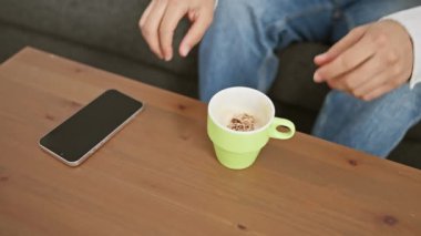 Sıradan giyinmiş bir adam akıllı telefonuyla meşgul ve yeşil kupayı oturma odasında tutuyor..