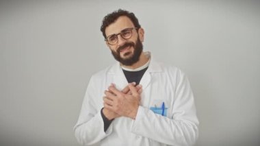 Mutlu orta yaşlı bir adam, bilim adamı üniforması giyiyor, elleri göğsünde gururlu ve minnettar bir jest sergiliyor. Beyaz bir arkaplanda izole haldeyken gülümsüyor.