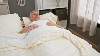Normal bir sabah rutinini yansıtan, rahat bir yatak odası ortamında esneyen olgun bir adam..