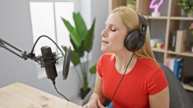 Modern bir stüdyoda mikrofon ve kulaklıklı kırmızı tişörtlü genç bir kadın podcast yapıyor..