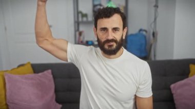 Orta yaşlı bir adam evinde güçlü kol kasları sergiliyor, beyaz tişörtle gösteriş yapıyor, sağlıklı yaşam tarzını, gücünü ve erkekliğini somutlaştırıyor.