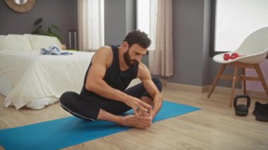 Sakallı bir adam, modern bir yatak odasında yoga minderine uzanıyor. Bu da sağlıklı ve aktif bir yaşam tarzını gösteriyor..
