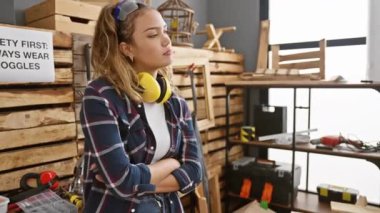 Kendine güvenen İspanyol kadın marangozluk stüdyosunda dinleniyor, genç ve güzel kulaklıkları, güvenlik gözlükleri, doğal gülümsemesi ve yan profil pozu var.