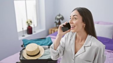 Tatilde kendini evinde gibi hisseden, güzel İspanyol bir kadın, otel odasında dinlenirken, akıllı telefonuyla mutlu bir şekilde sohbet ediyor, bavulunu sabah yolculuğuna hazırlıyor..