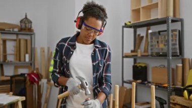 Kapalı atölyede çekiç ve koruyucu aletlerle çalışan genç bir kadın.