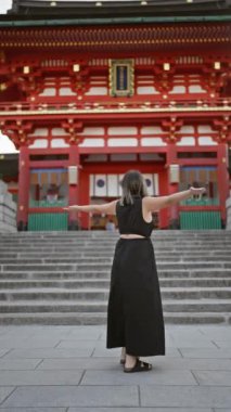 Gözlüklü neşeli İspanyol kadın, özgürlüğü kucaklıyor, gülümsüyor ve Kyoto, Japonya 'daki fushimi inari taisha türbesine bakıyor.