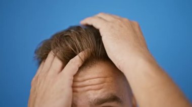 Temiz mavi bir arkaplan karşısında şık bir saç stili olan genç bir İspanyol 'un yakın plan fotoğrafı. İfade eden gözlerini ve saçlarını şekillendiren ellerini yakalıyor..