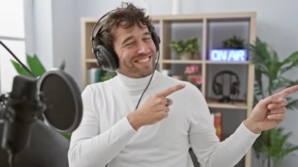 Cheerful Young Hispanic Man Radio Studio Joyfully Pointing Side While — Stock Video