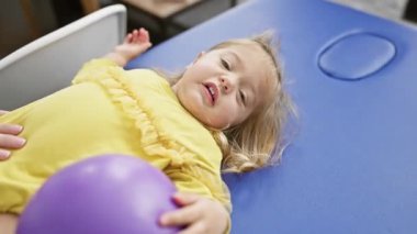 Sarı elbiseli genç bir kız rehabilitasyon kliniğinde mor bir topla tedavi görüyor..