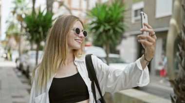 Gülümseyen kadın güneşli şehirde selfie çekiyor.