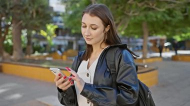 Şehir caddesinde dururken akıllı telefon kullanan genç bir kadın..