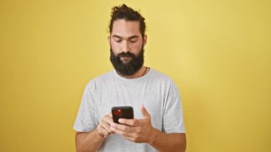 Sarı duvara karşı akıllı telefon kullanan sakallı, endişeli, genç bir İspanyol.