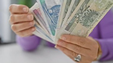Olgun bir kadın ofis masasındaki zloti banknotlarını sayıyor, finansal planlama ve bütçe kavramını yansıtıyor..