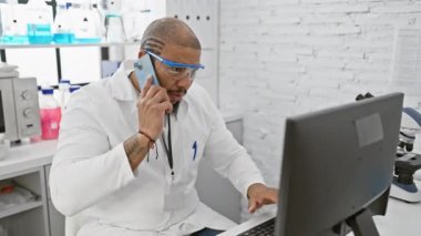 Laboratuvardaki sakallı bilim adamı bilgisayar ve telefon konuşmalarıyla birden fazla iş yapıyor..