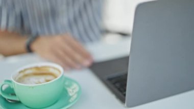 Bir adam açık hava avlusunda dizüstü bilgisayarıyla çalışırken kahveden zevk alır..