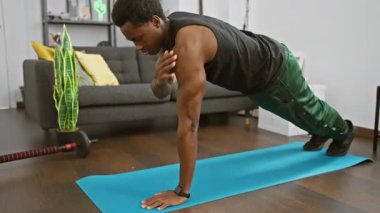 Modern bir oturma odasında yoga minderinde şınav çeken Afrikalı Amerikalı bir adam.