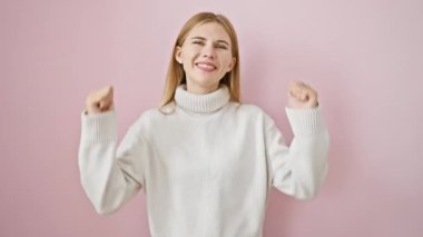 Neşeli galip! Güzel sarışın kız ayakta duruyor, baş parmak işareti yapıyor. Başarı karşısında geniş bir gülümseme, pozitif titreşimler yayıyor. pembe arkaplanda izole edilmiş duruyor.