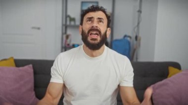Stresli orta yaşlı adam öfkeyle patlıyor, deli ve sinirli, hayal kırıklığı içinde bağırıyor! Kolları havada, agresif bir ifadeyle, evinde, beyaz bir tişört giyerken..