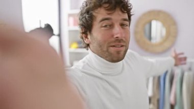 Balıkçı yaka yakalı yakışıklı genç adam arka planda şık bir gardırop olan parlak bir elbise odasında özçekim pozu veriyor..